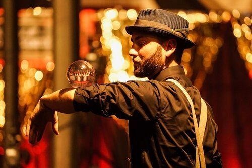 A man in a hat is juggling a glass ball.