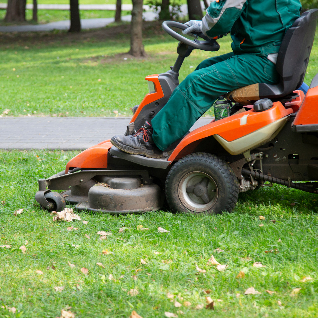 A man is riding a lawn mower in a park.