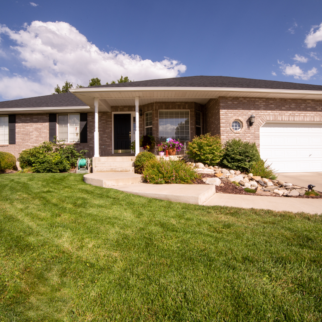 A brick house with a white garage door and a large lawn in front of it.