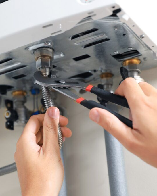 Hands using pliers and wrench to repair a white water heater mounted on a wall — Firefly Connections In Teralba, NSW