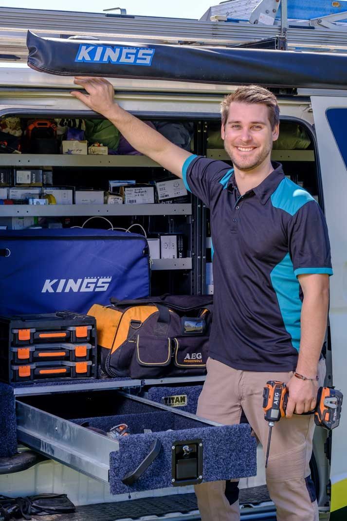 Man smiling next to open van, holding drill, arm raised. Van interior shows tools — Firefly Connections In Mayfield, NSW