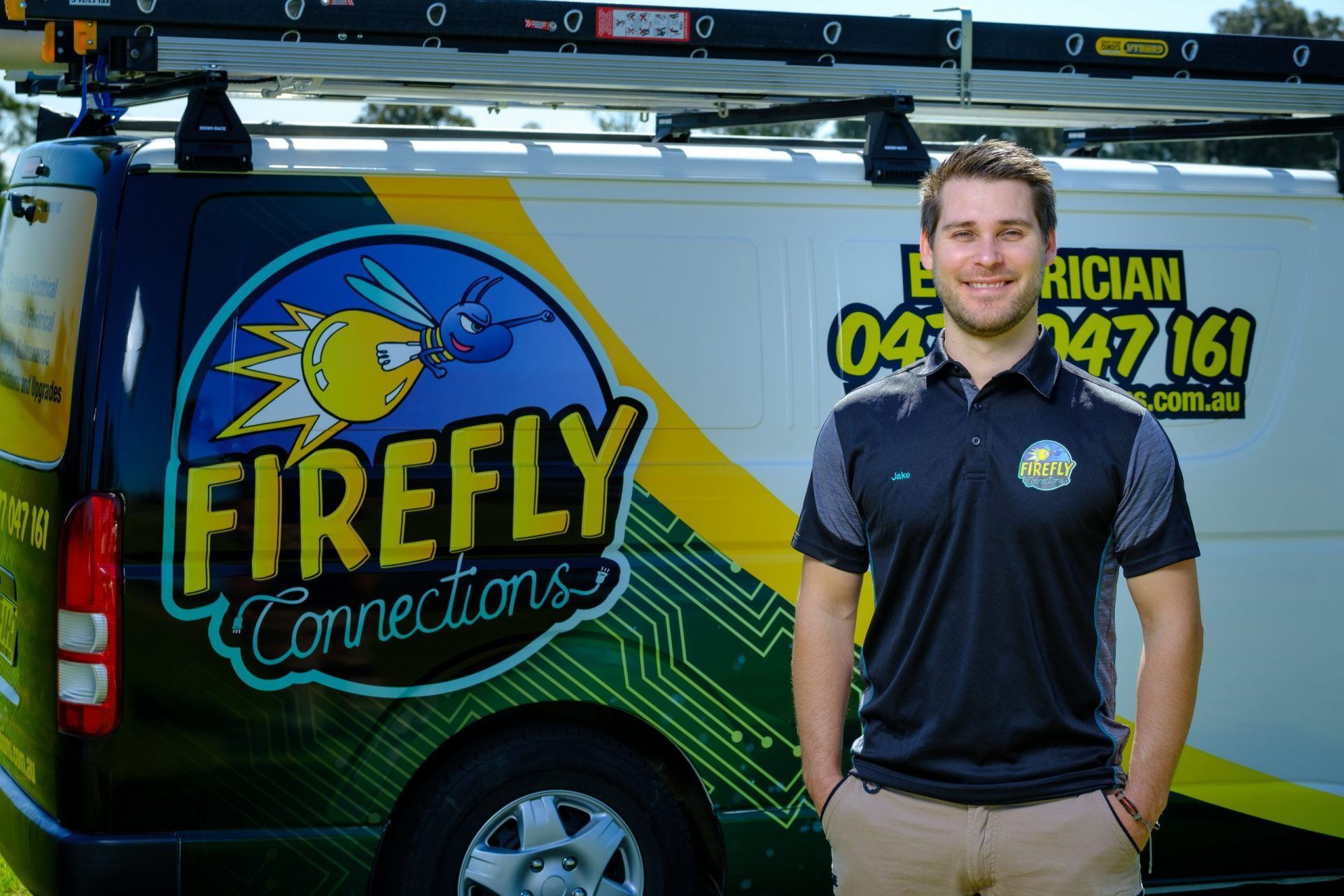 Smiling man in uniform stands beside a Firefly Connections electrician van — Firefly Connections In Mayfield, NSW