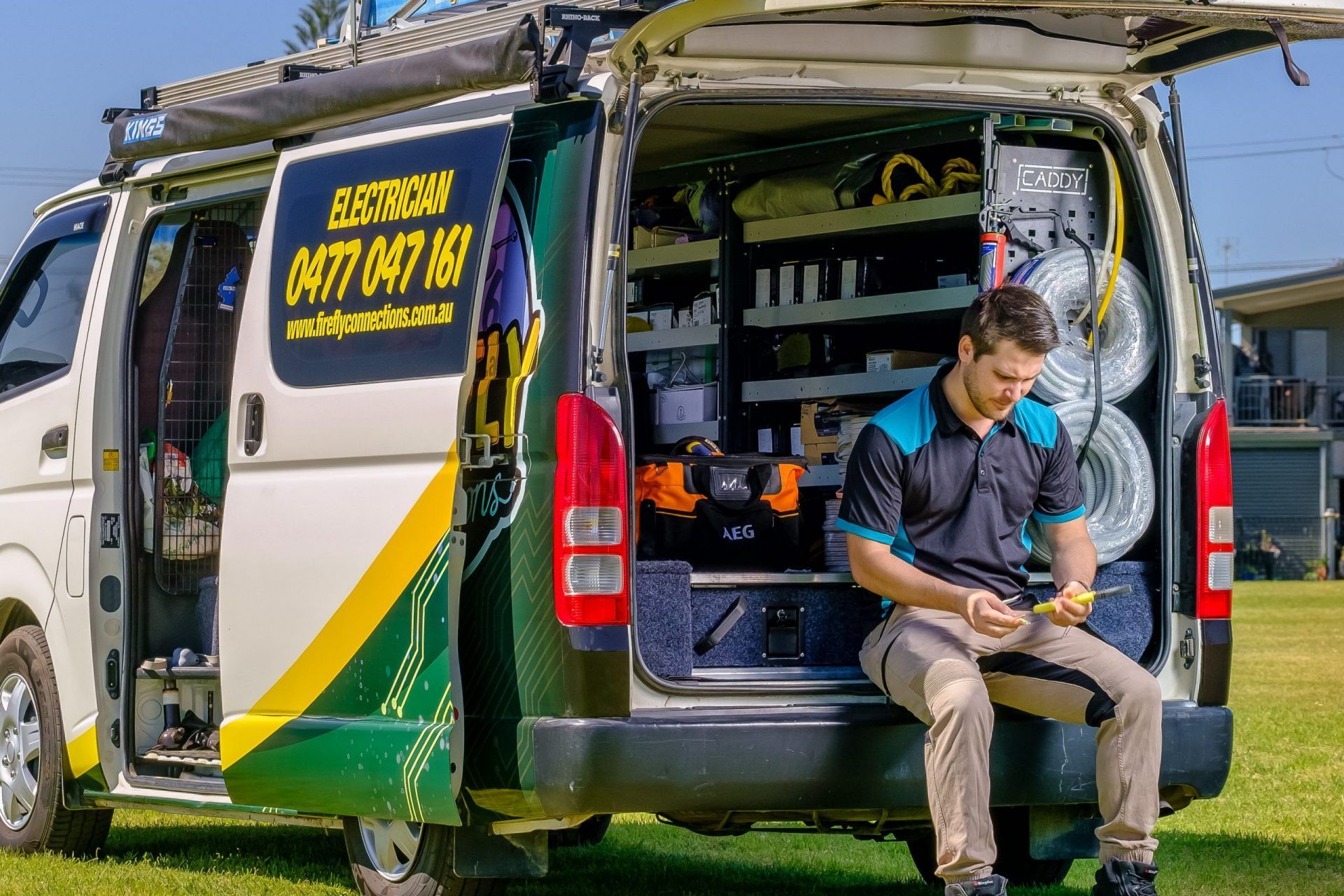 Electrician seated in the open back of a van, working with tools — Firefly Connections In Mayfield, NSW