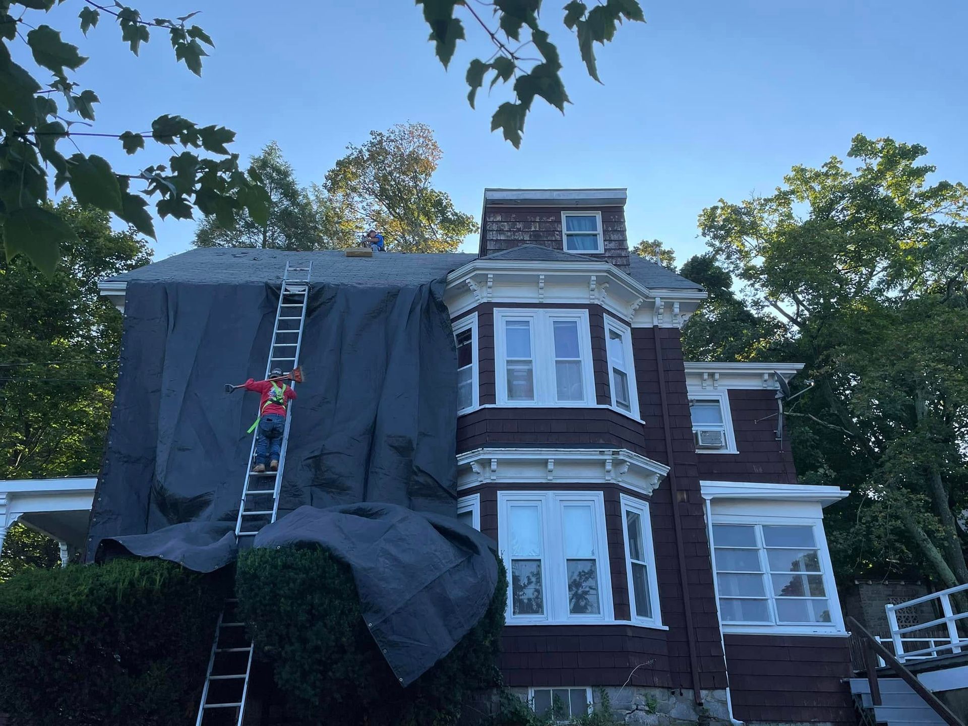A man on a ladder is working on the roof of a house
