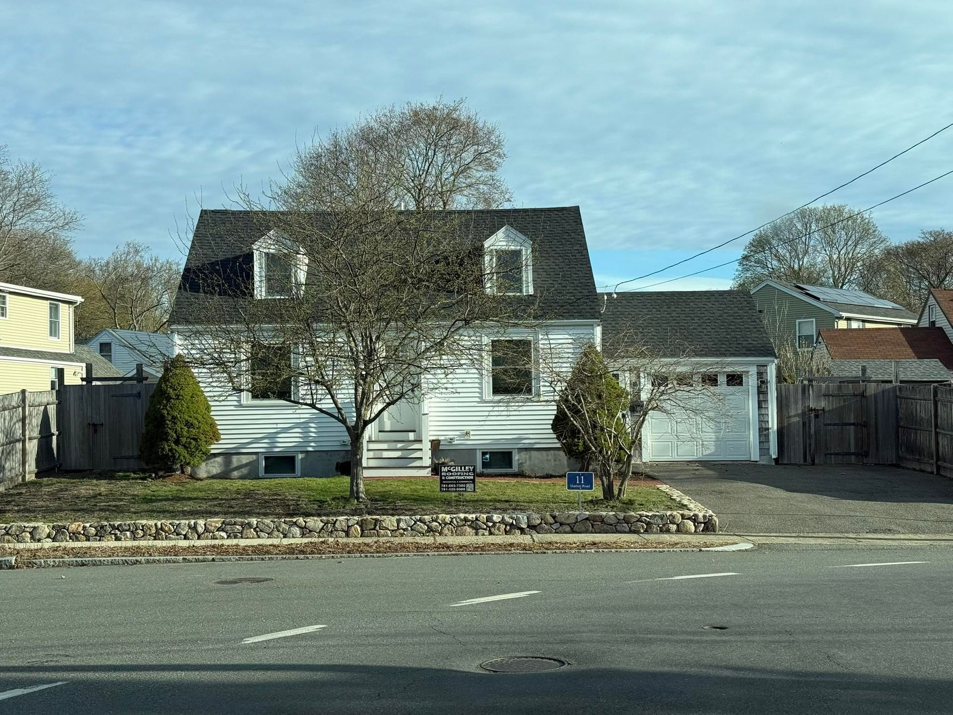 A white house with a black roof is sitting on the corner of a street.
