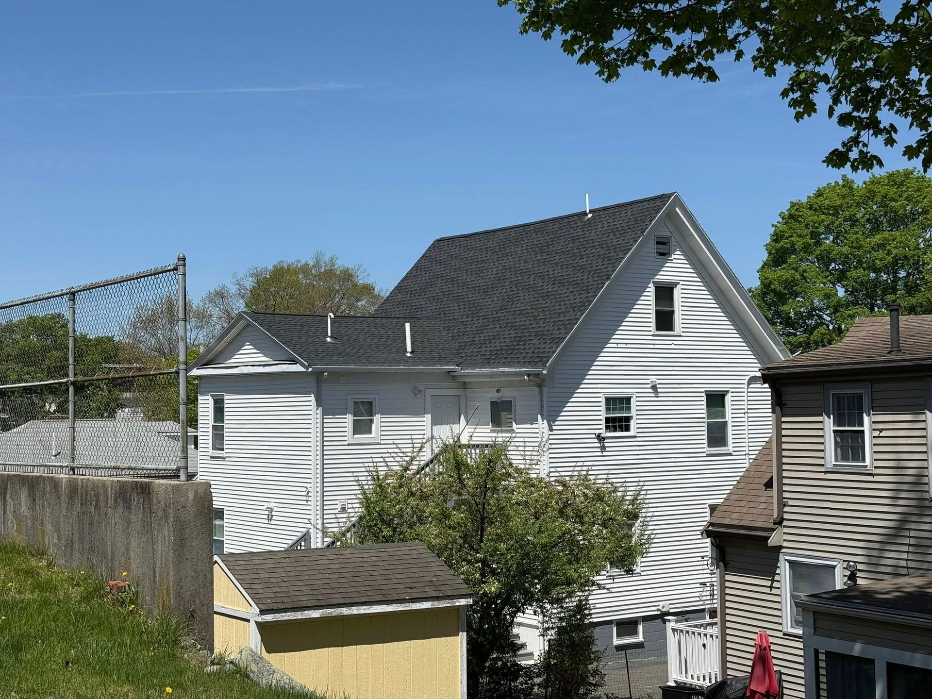 A white house with a black roof and a yellow shed