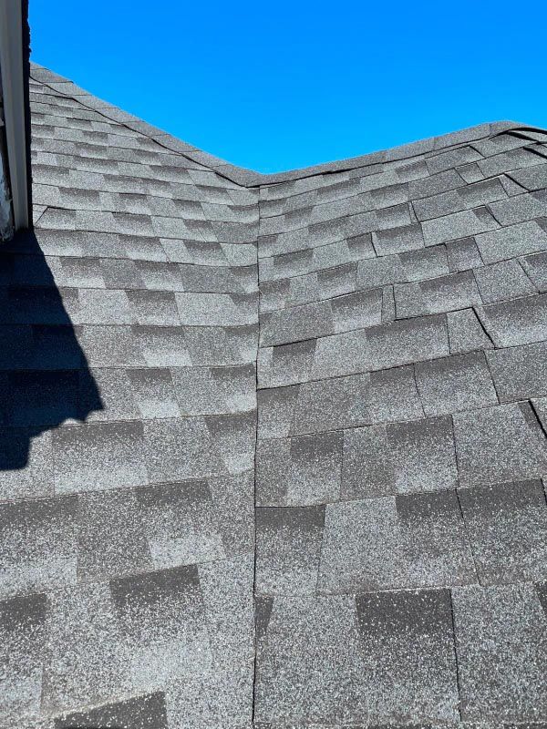 A close up of a roof with shingles and a blue sky in the background.