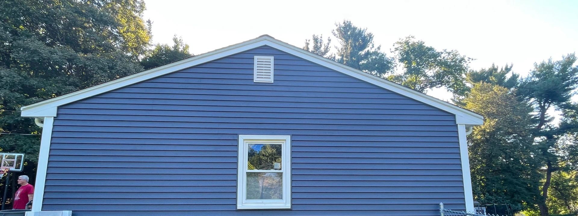 A blue house with a white trim and a window is surrounded by trees.