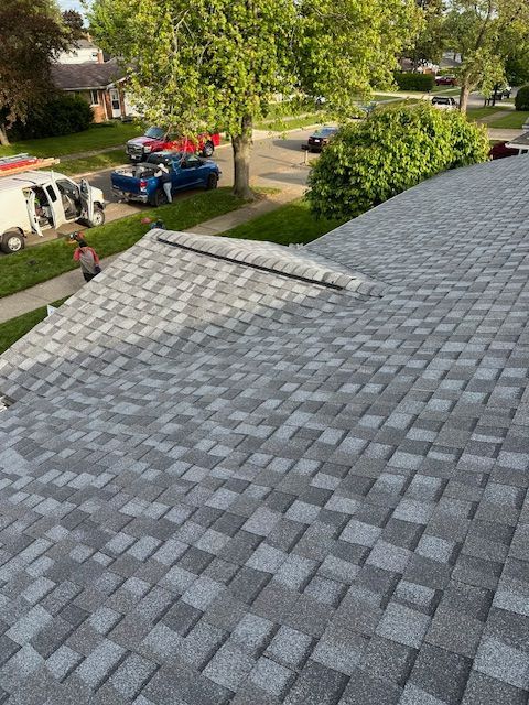 A view from a grey shingled roof looking down at a street with parked vehicles and residential trees. A view from a grey shingled roof looking down at a street with parked vehicles and residential trees.