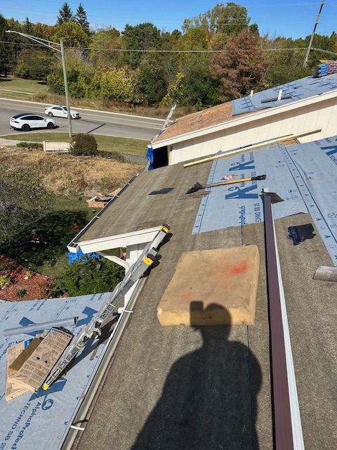 A roof under construction featuring exposed sheathing, blue underlayment, an extension ladder, and construction materials. A roof under construction featuring exposed sheathing, blue underlayment, an extension ladder, and construction materials.
