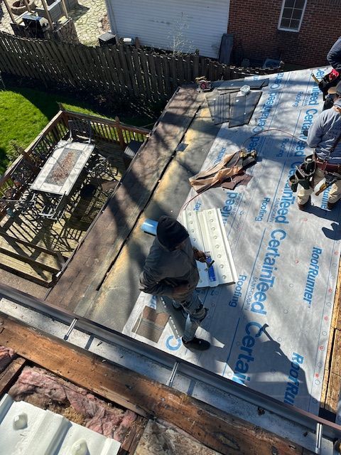 A roof under construction featuring exposed sheathing, blue underlayment, an extension ladder, and construction materials.