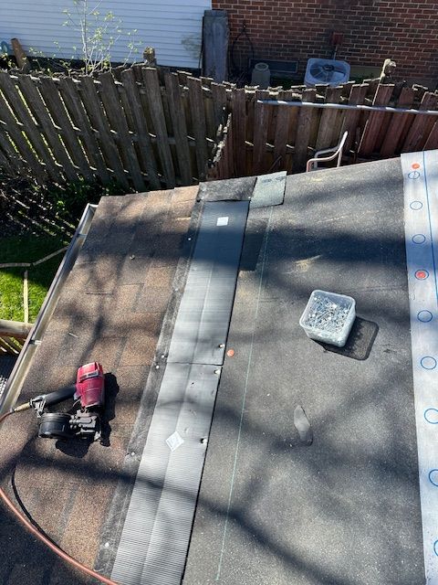 Rooftop with gray shingles, a pink-and-black tool, and a vent near a wooden fence.
