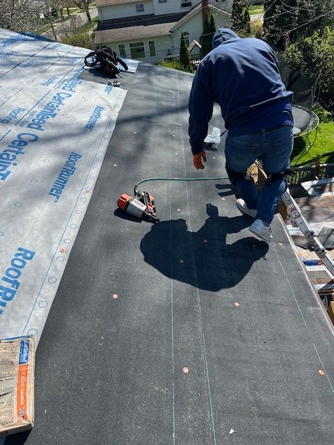 Worker using a roofing nailer on a roof underlayment during roof installation