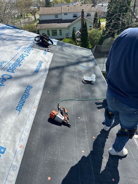 Worker on a rooftop installing roofing material with tools and insulation sheets nearby.