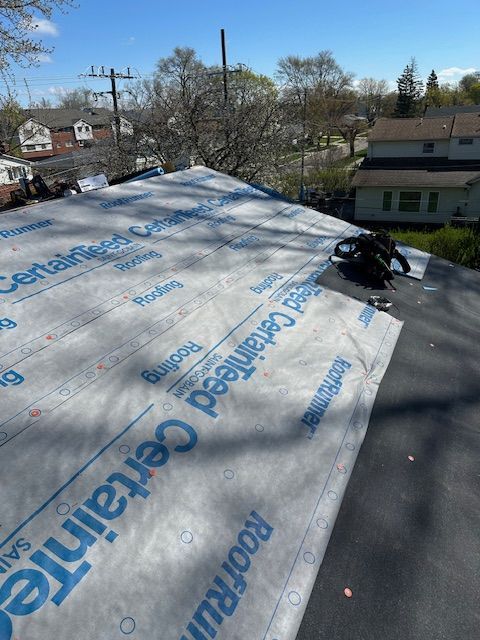 A high-angle view of a brown shingled roof, with three people standing on the ground near a suburban house.
