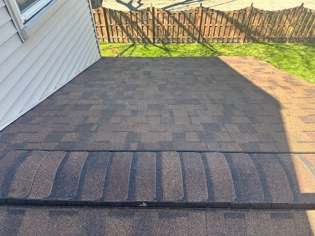 Back patio with paver stones, white siding, and a fenced grassy yard in sunlight.