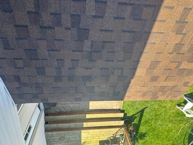 Backyard view of a lawn beside a house and deck, with a brick wall and patio chair in sunlight