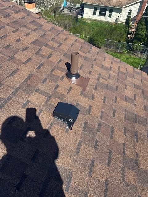 Rooftop view of brown shingle shingles with a vent pipe, black box, and photographer’s shadow.