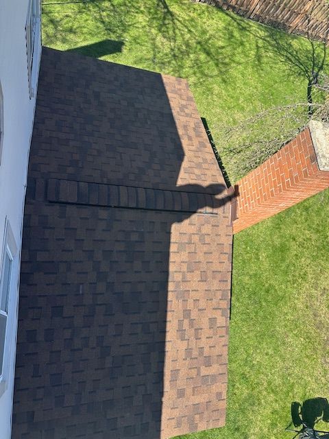 Aerial view of a dark shingled roof beside a brick chimney and green lawn.