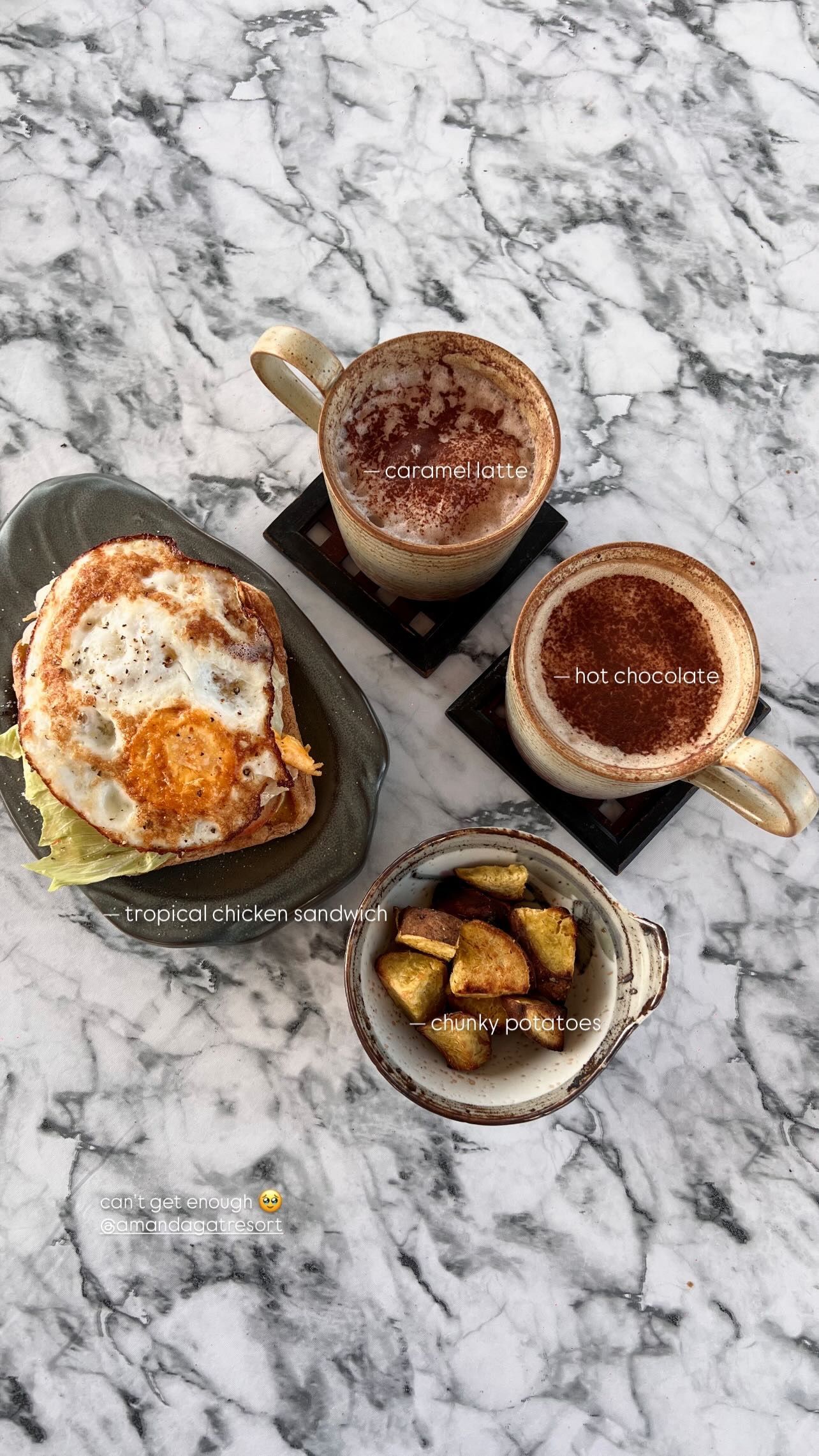 A top-down view of breakfast: a fried egg on toast, two mugs of coffee, and a small bowl of potatoes on a marble table.