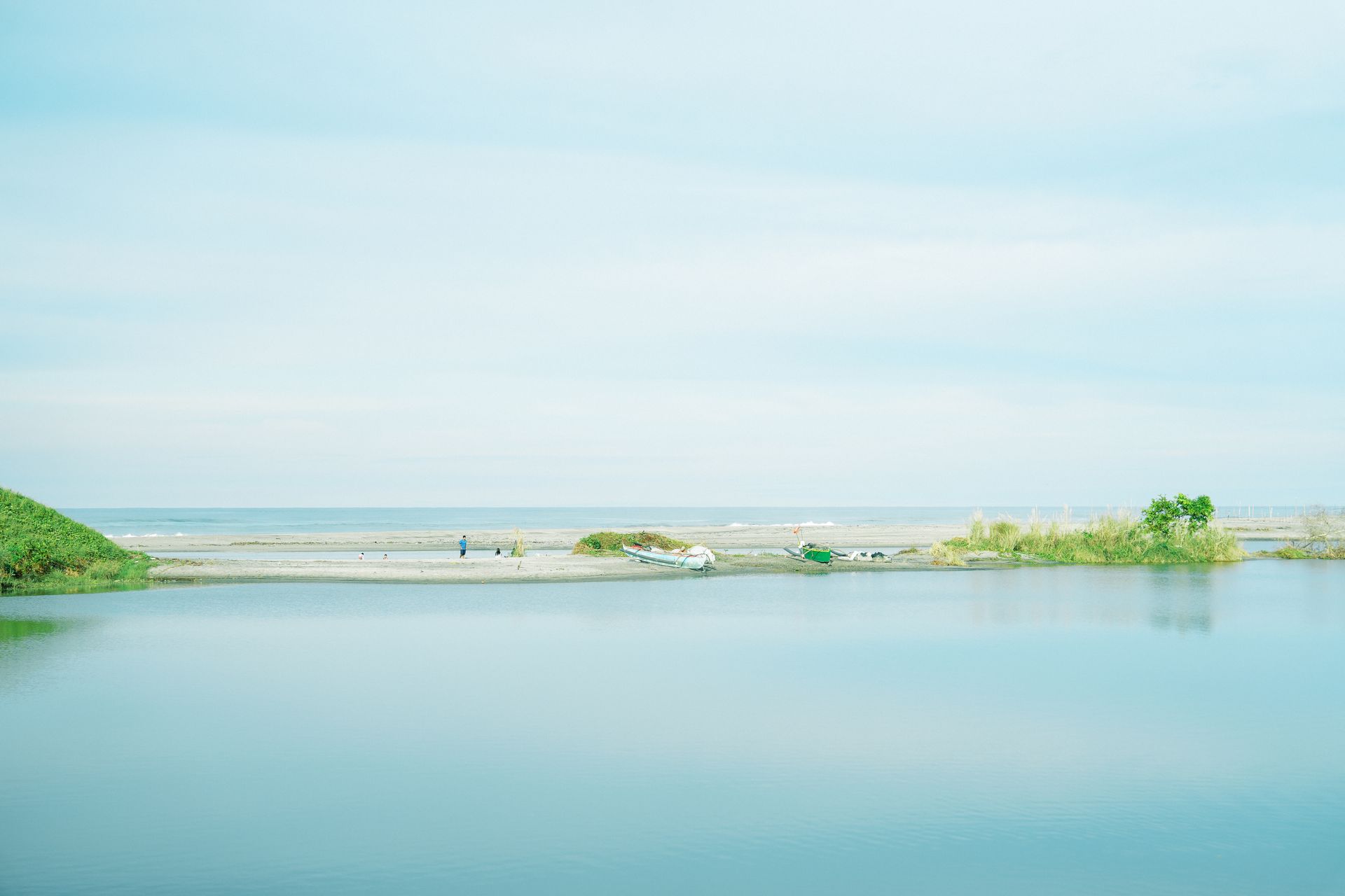 Calm, light blue water reflecting a shore. A strip of land separates water and sky.