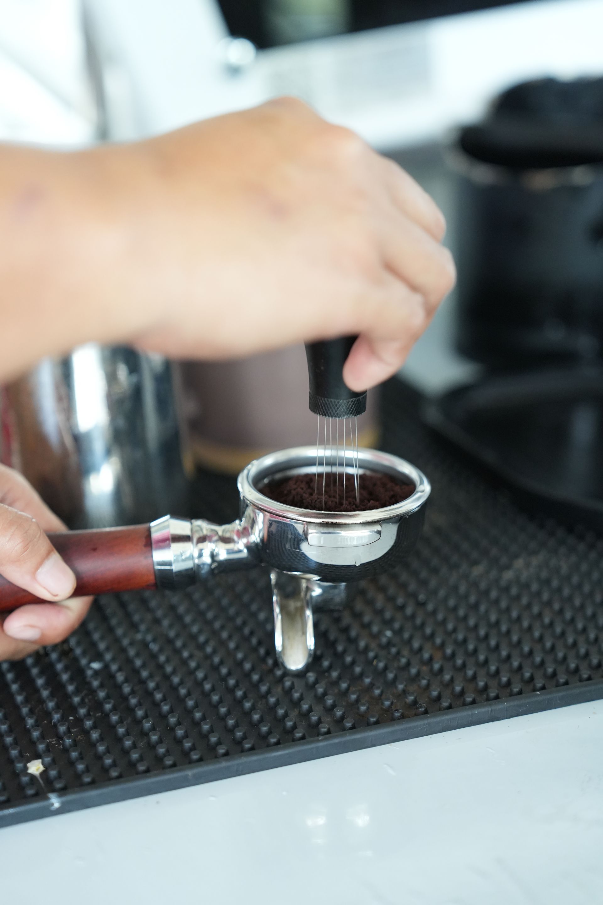 Person tamping ground coffee in a portafilter, preparing espresso.