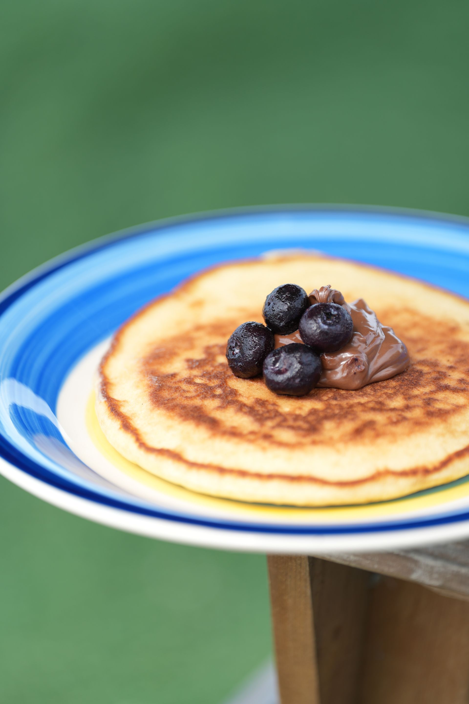 Pancake stack topped with blueberries and a dollop of chocolate spread on a blue-rimmed plate.
