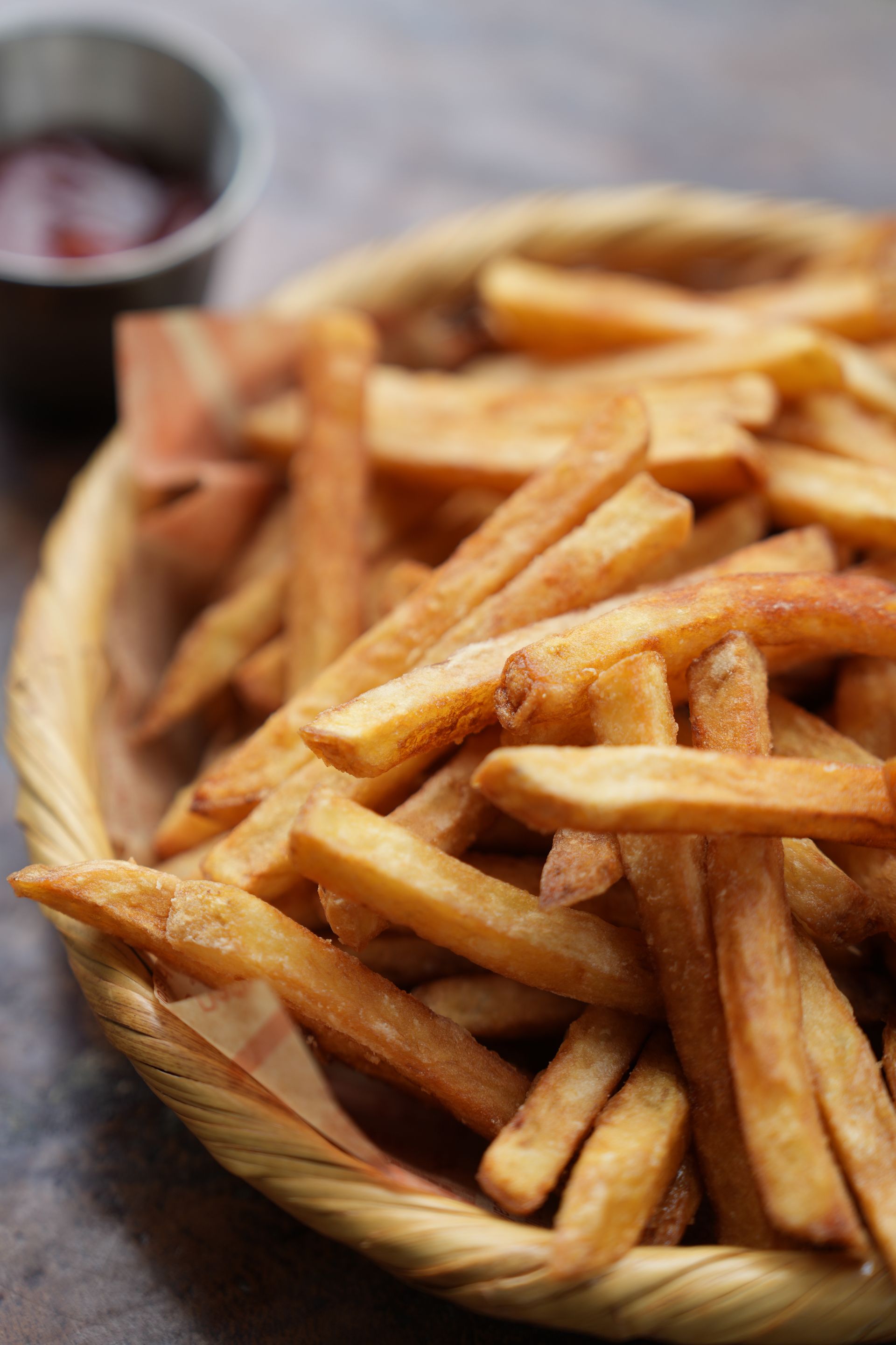 Golden french fries in a woven basket, ketchup cup in background.