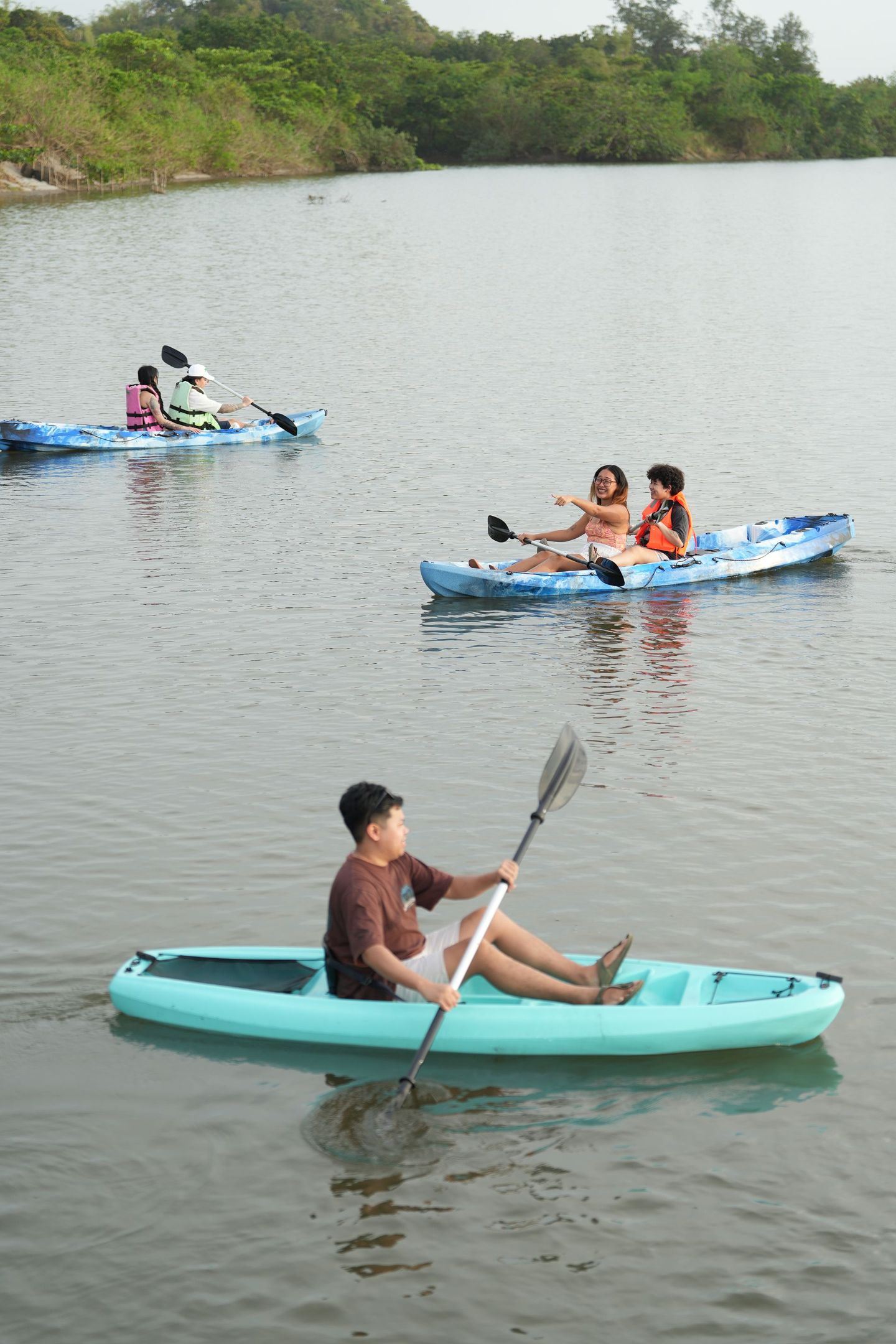 People kayaking on calm water. Three kayaks are visible; one is teal, two are blue.