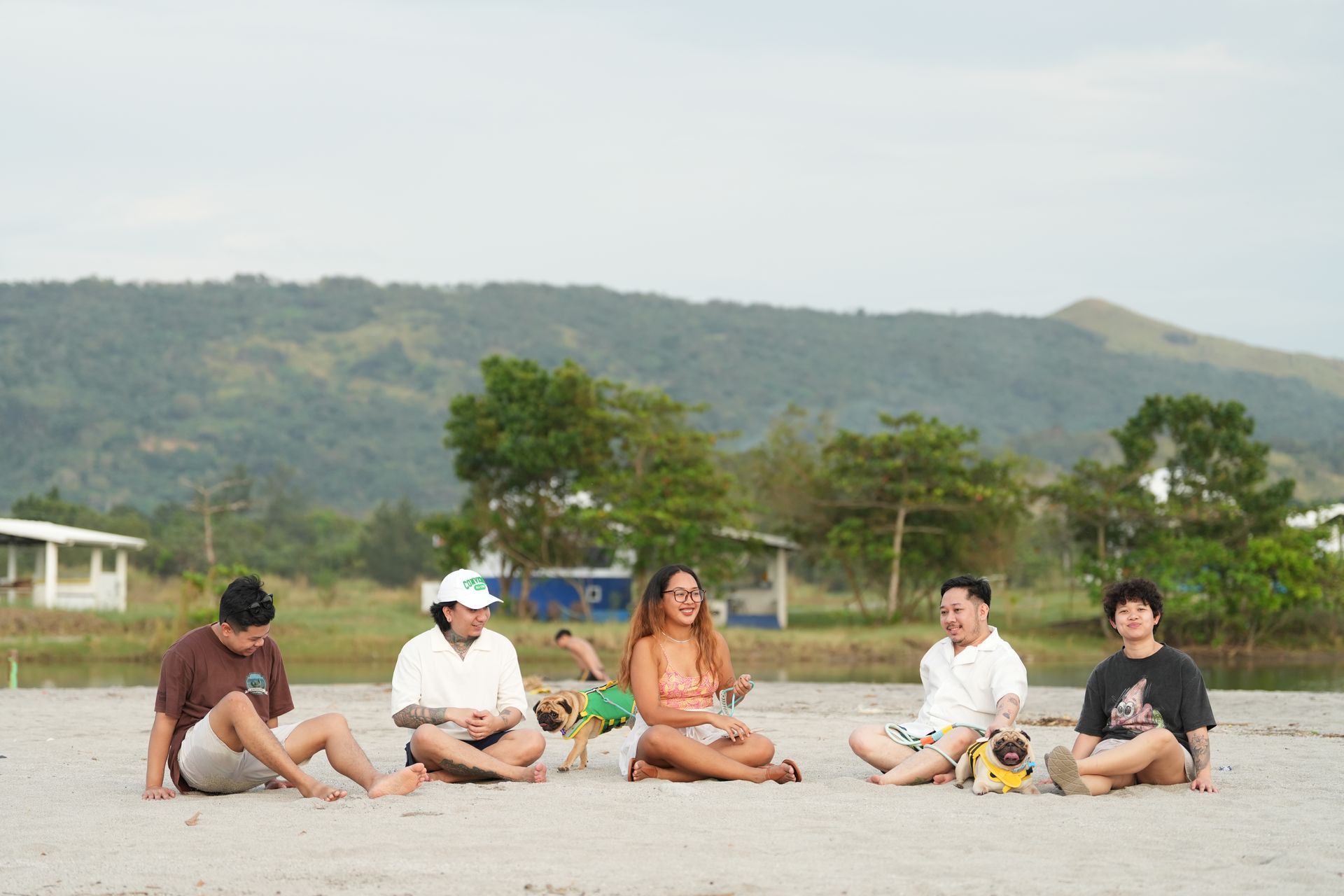 Five people and two dogs sit on a beach with a mountain backdrop.