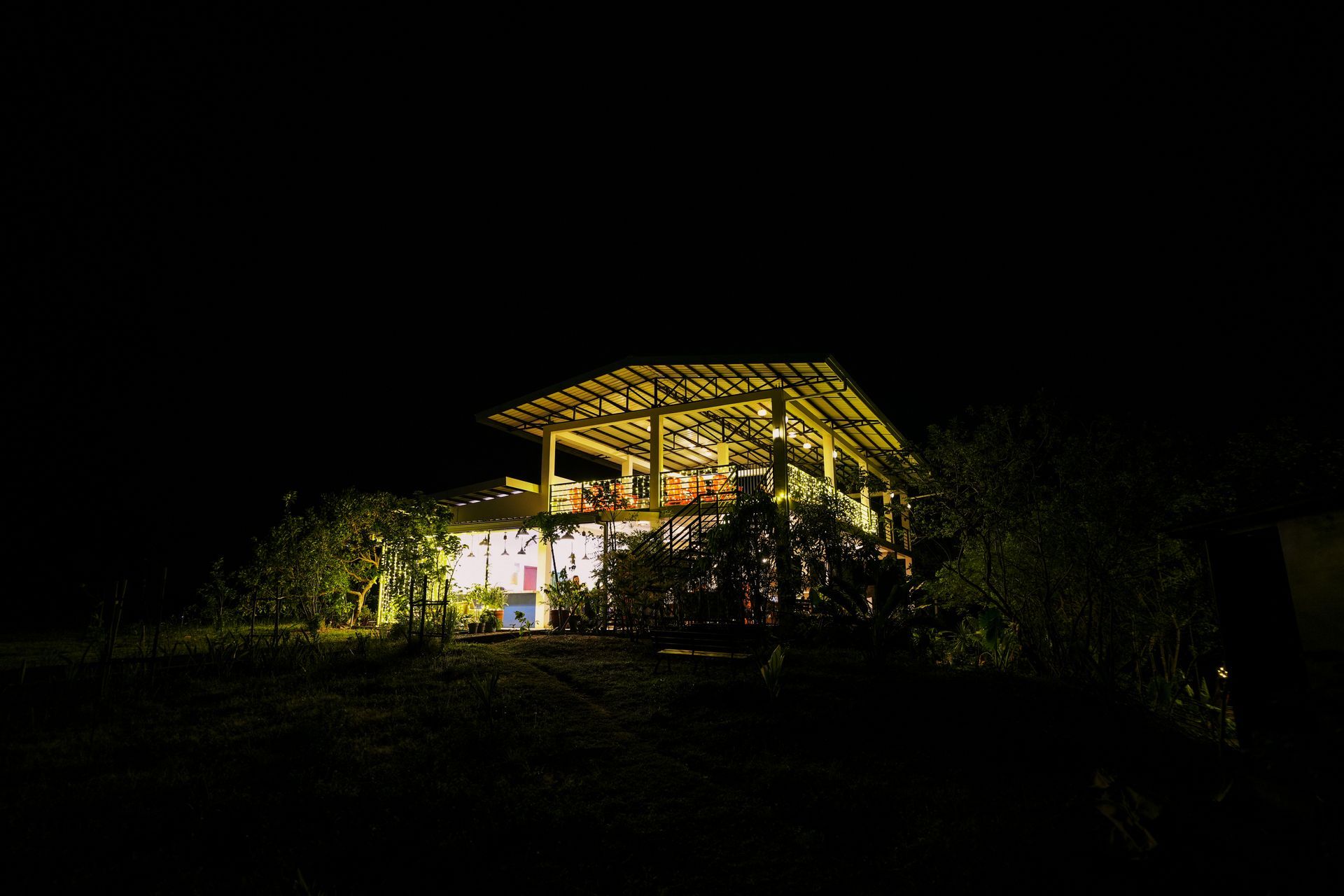 House lit at night, set on a hill with surrounding trees.