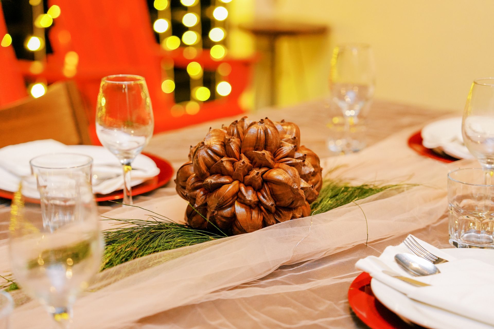 Festive dining table set with glassware, plates, silverware, and a large brown centerpiece.