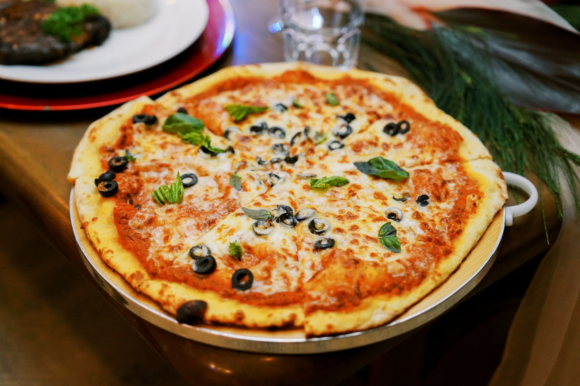 Pizza on a wooden serving board, with tomato sauce, cheese, olives, and basil.