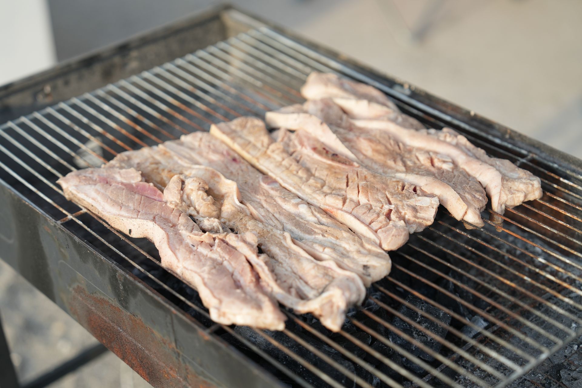 Raw pork ribs grilling on a barbecue, outdoors.