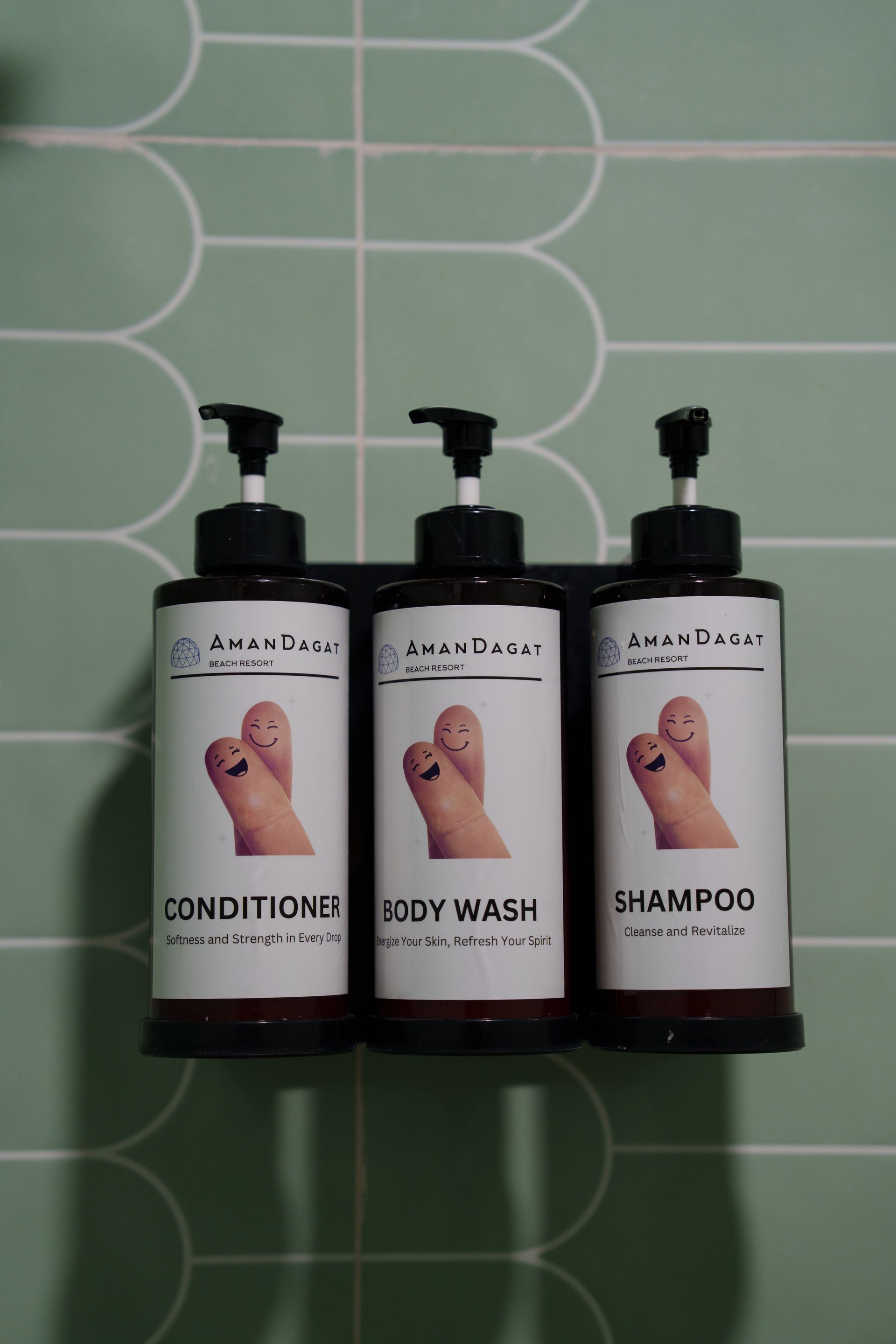 Three shampoo bottles with finger-like faces in a wall holder on a green tiled wall.