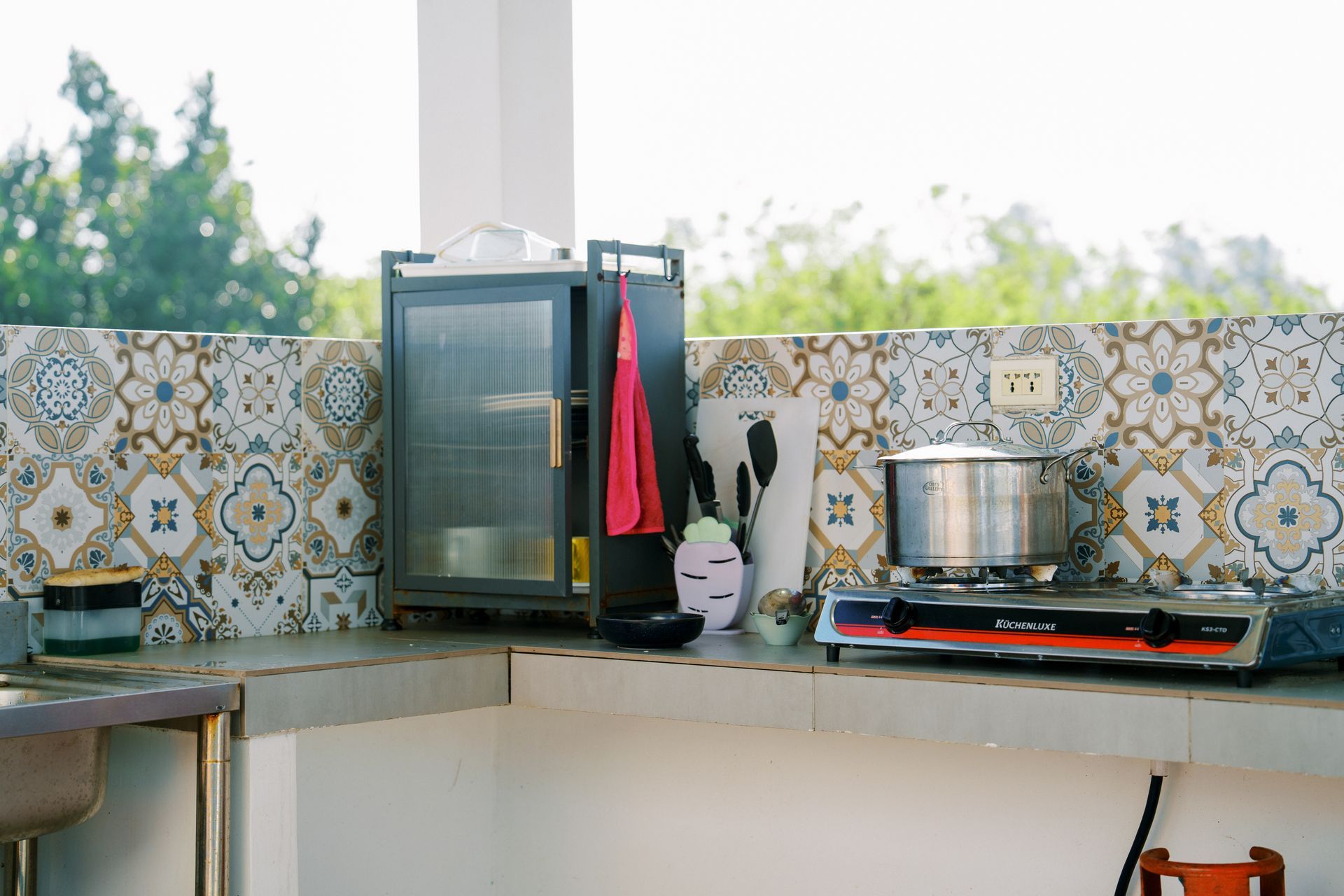 Outdoor kitchen countertop with a stove, cabinet, and decorative tiles.