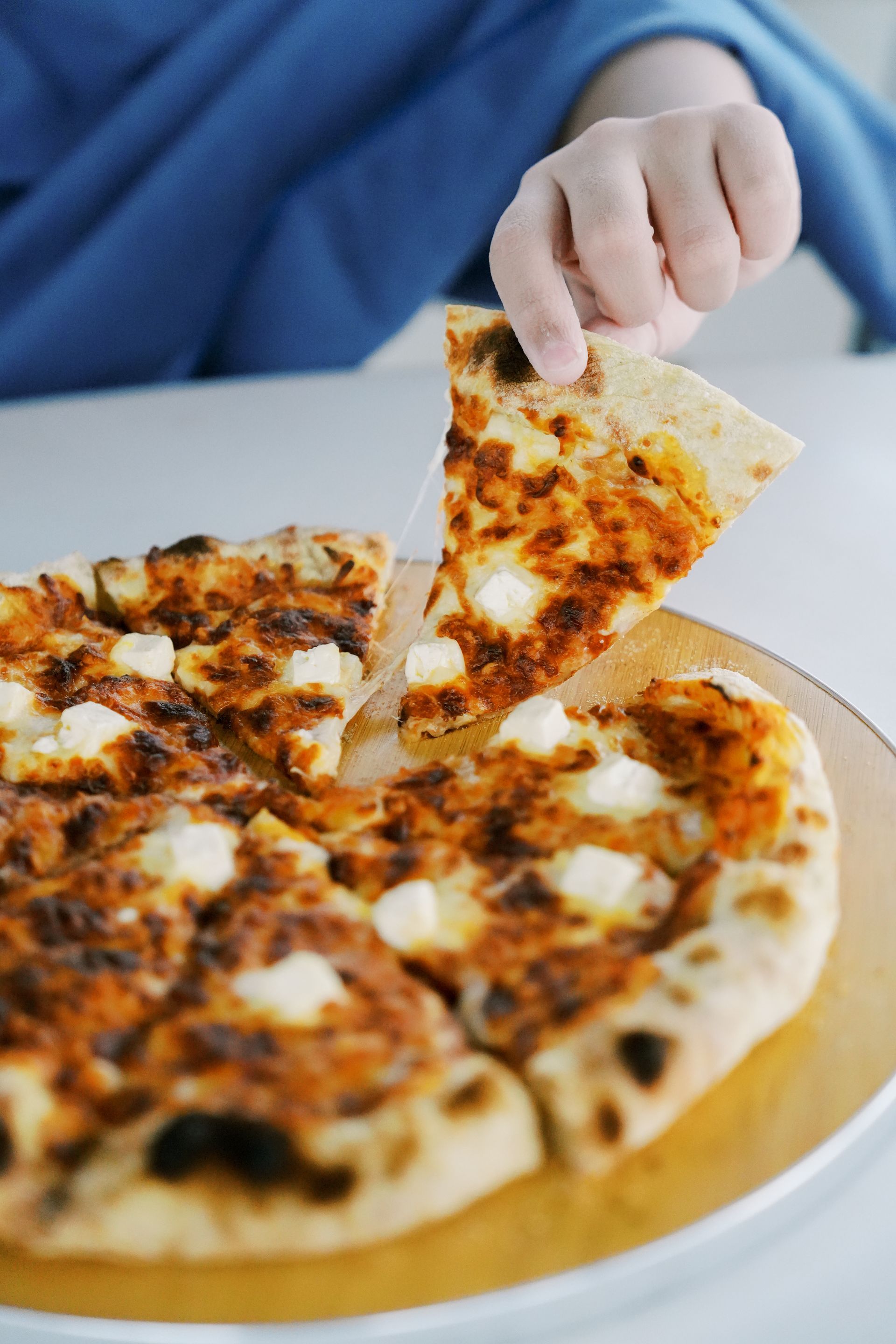 Hand reaching for a slice of pizza topped with cheese on a wooden board.