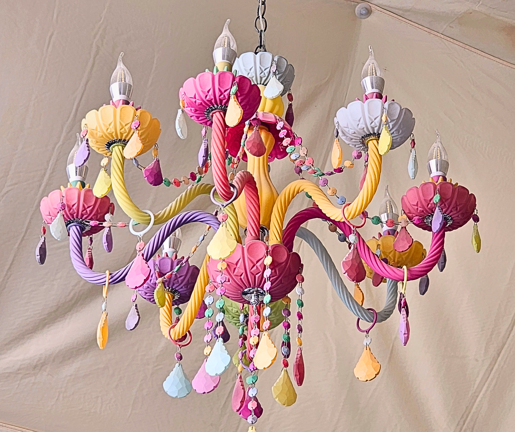 Colorful, whimsical chandelier with swirling arms, decorated with hanging jewels and frosted, layered flower shapes.