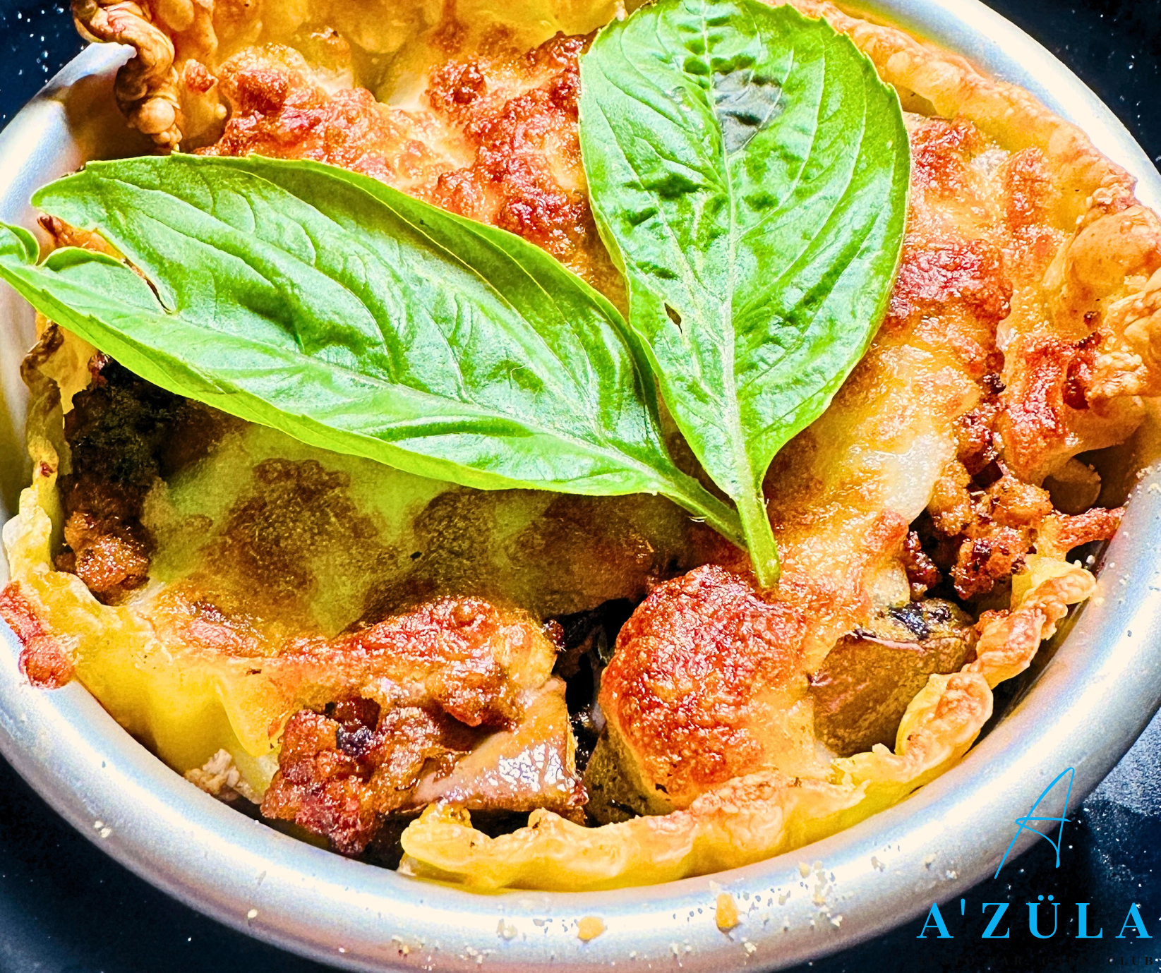 Mini savory tart with crispy crust, meat filling, and basil leaves on top.