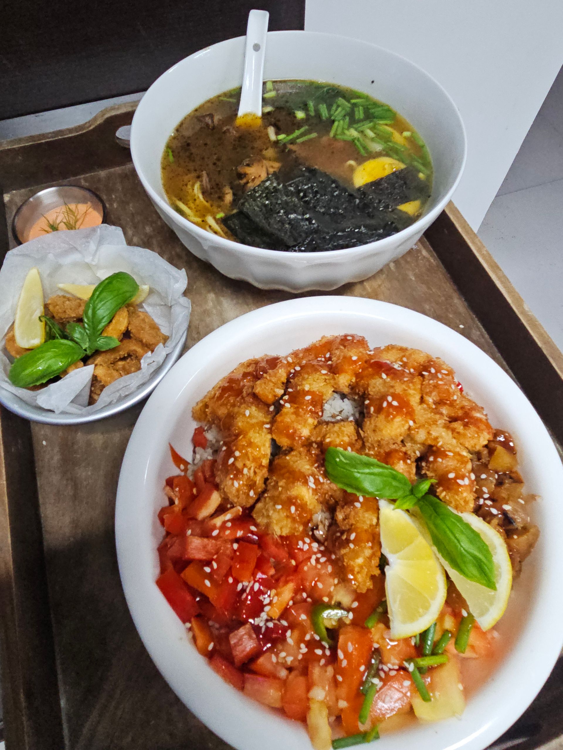 Tray with miso soup, fried dish, and teriyaki chicken bowl with vegetables and lemon.