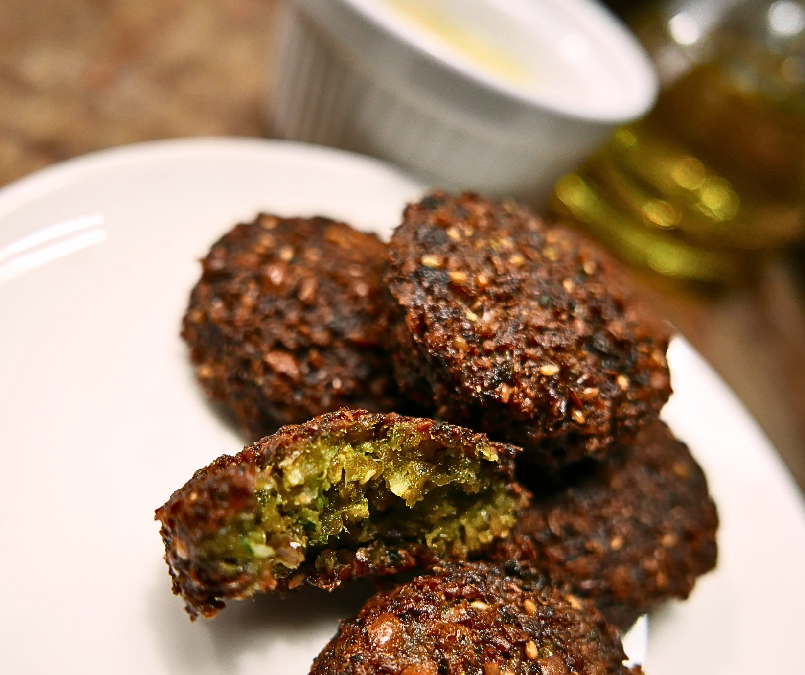 Close-up of crispy falafel on a white plate, one broken open to show a green interior.