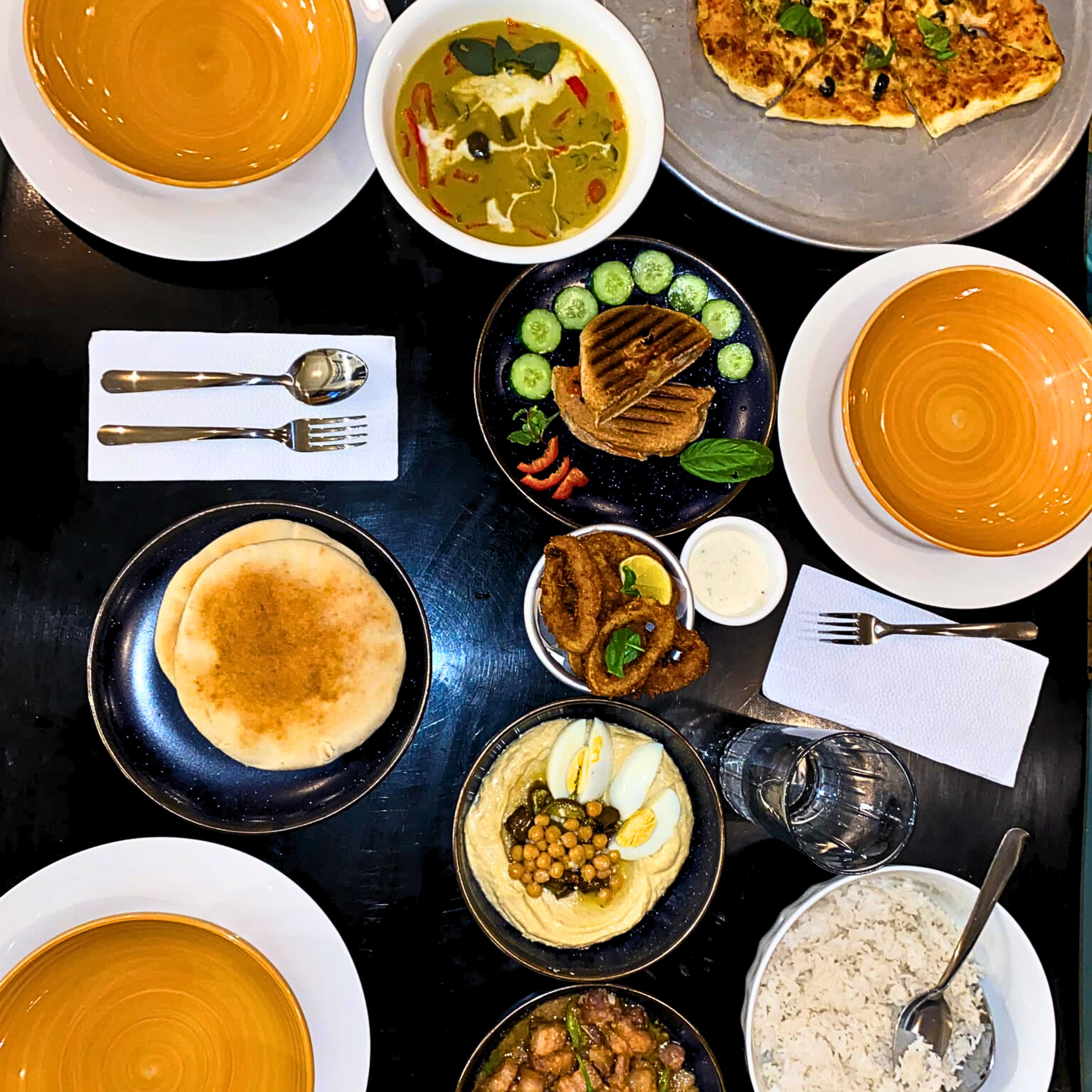 Overhead view of a table set with various Middle Eastern dishes: soup, hummus, pita, and rice.