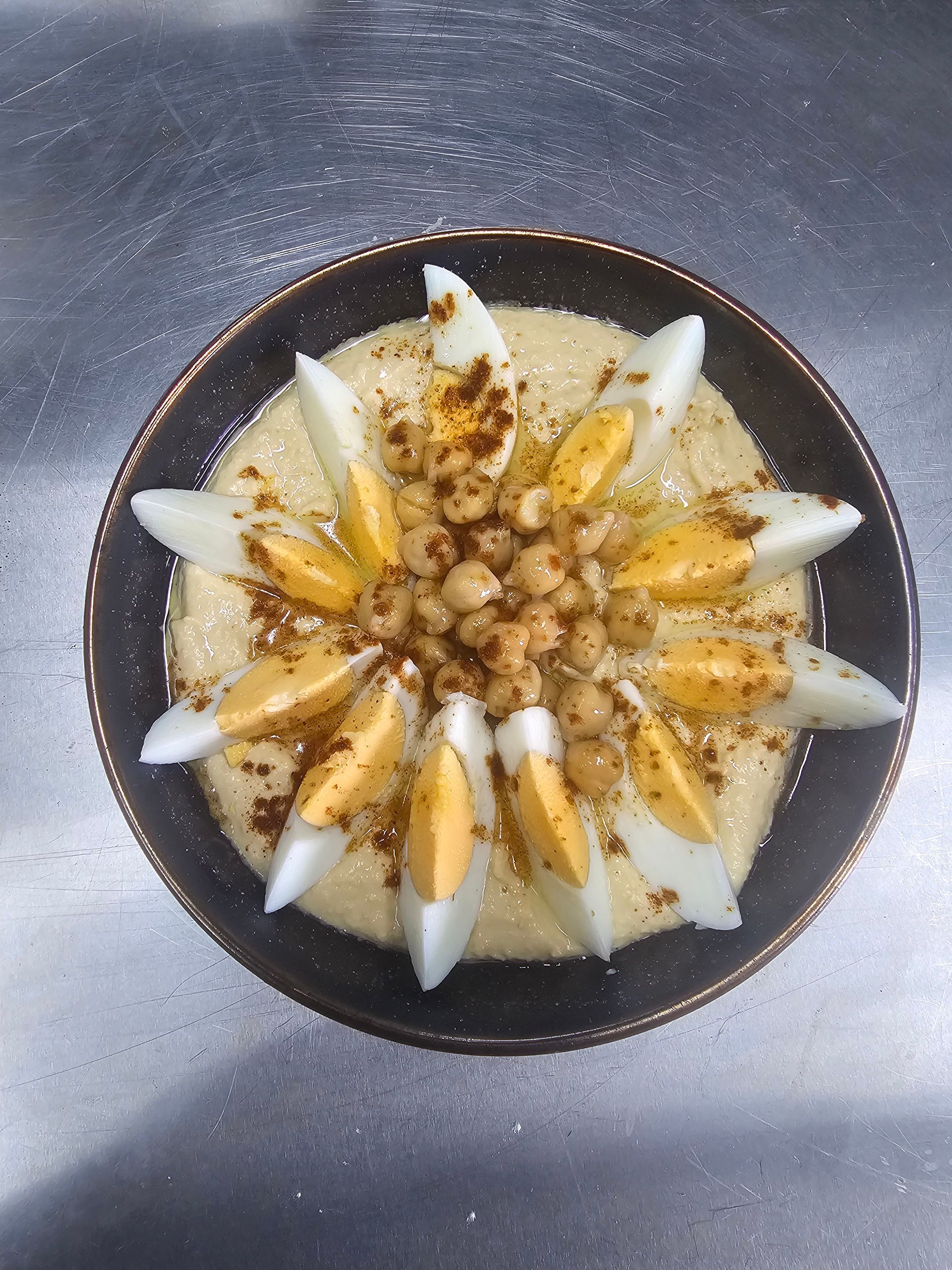 Hummus dish topped with egg wedges, chickpeas, and spice, arranged on a dark plate.