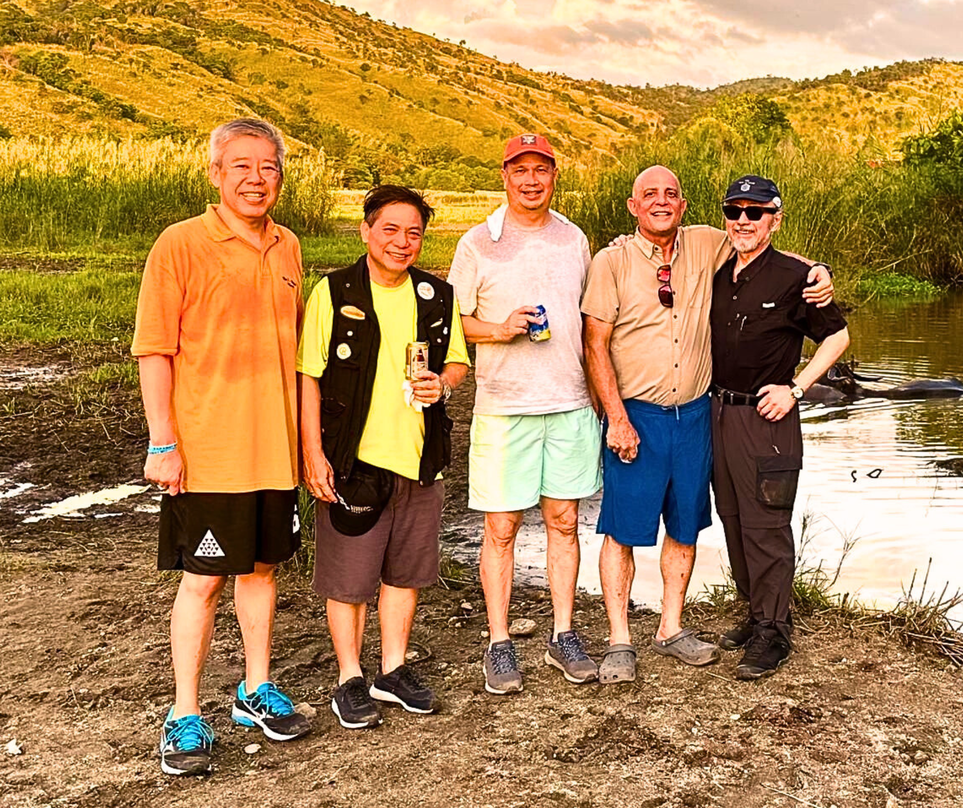 Five men standing near a river with a hilly background.