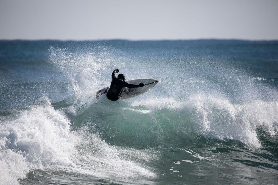 Surfer in black wetsuit riding a wave, creating a splash in the ocean.