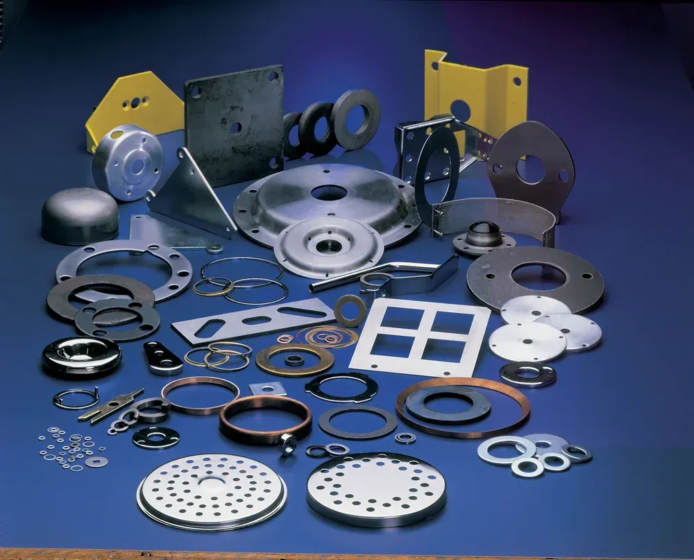 Assorted metal stamped parts, including washers, brackets, and discs, arranged on a blue surface.