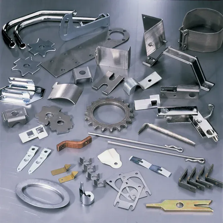 Various shiny, metal fabricated parts arranged on a light gray surface, showcasing different shapes and sizes.