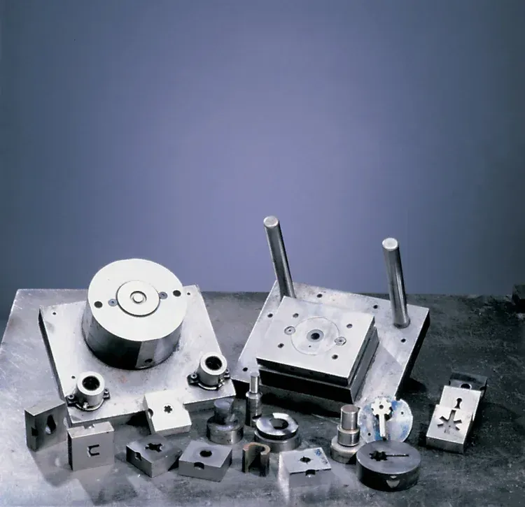 Various metal machine parts on a reflective surface, arranged against a blue-gray background.