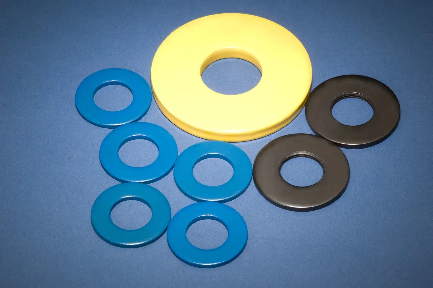 Assorted colorful washers: blue, yellow, and black, arranged on a blue surface.