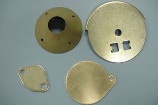 Four brass-colored metal parts with various shapes and cutouts, likely for mechanical assembly.